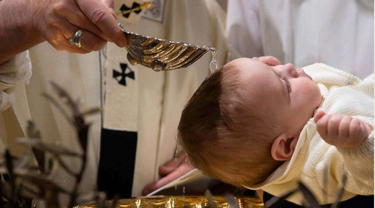 Priest holds a communion spoon over a baby during a church baptism ceremony