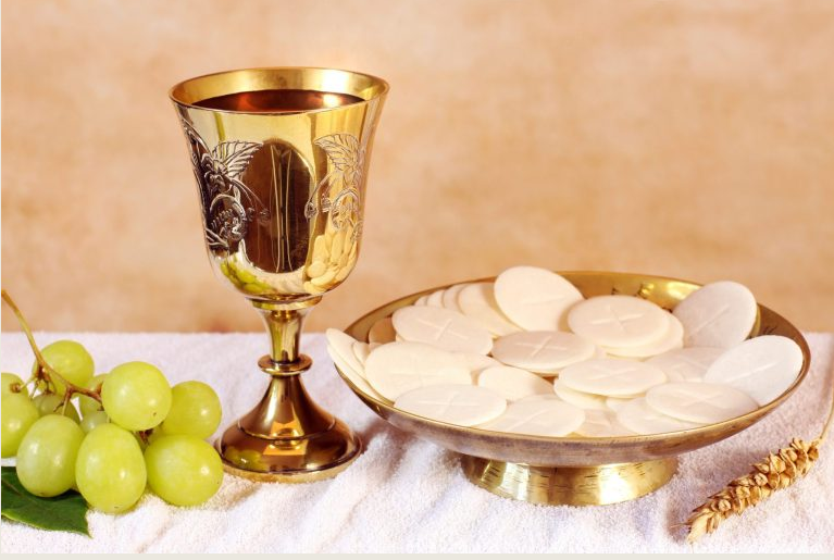Gold chalice, white communion wafers on a plate, and green grapes on a white cloth