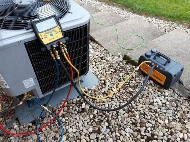 An HVAC technician using diagnostic equipment on an air conditioning unit. Outdoor setting.