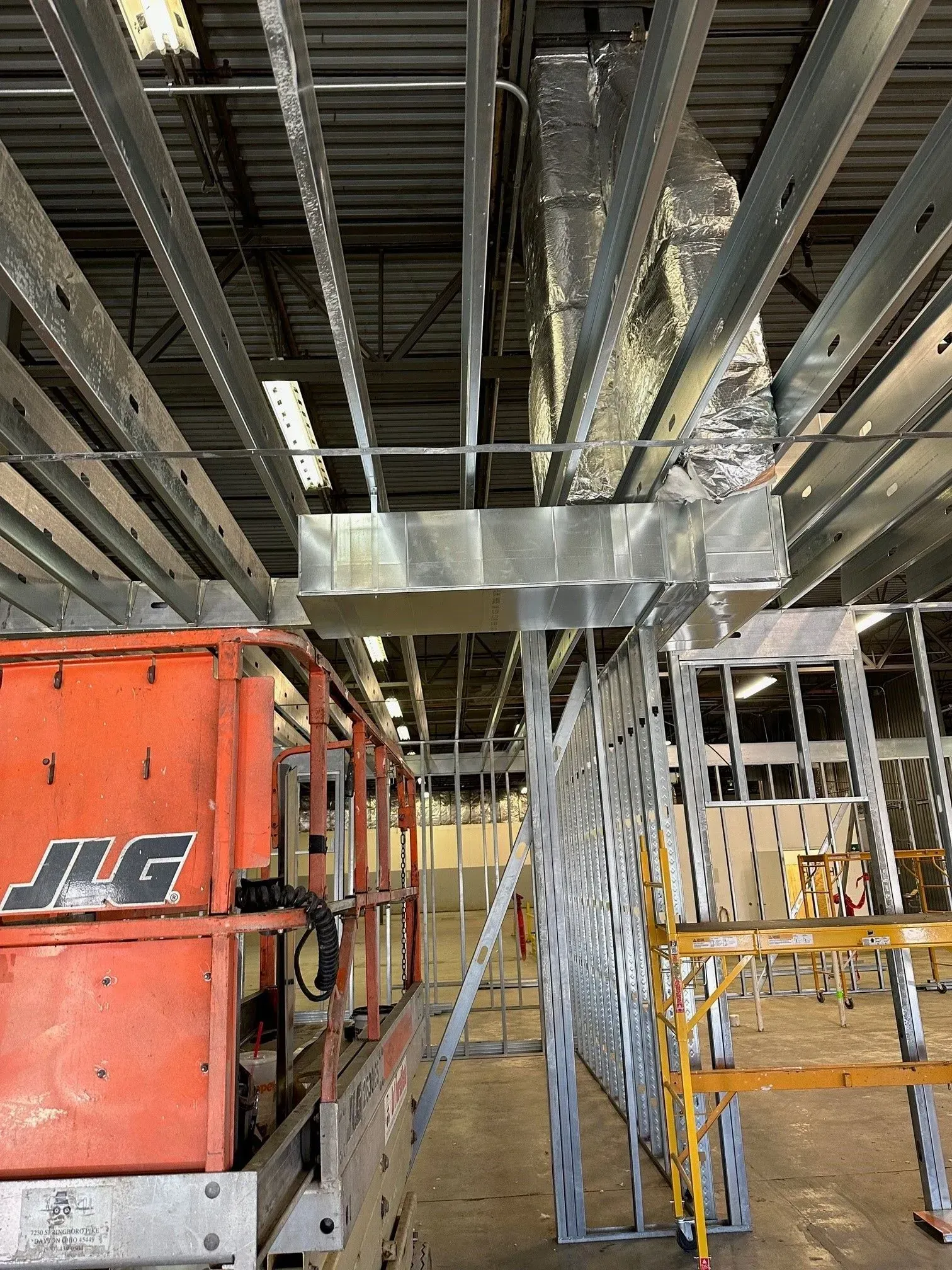 Construction site with metal framing, HVAC ductwork, and an orange lift.