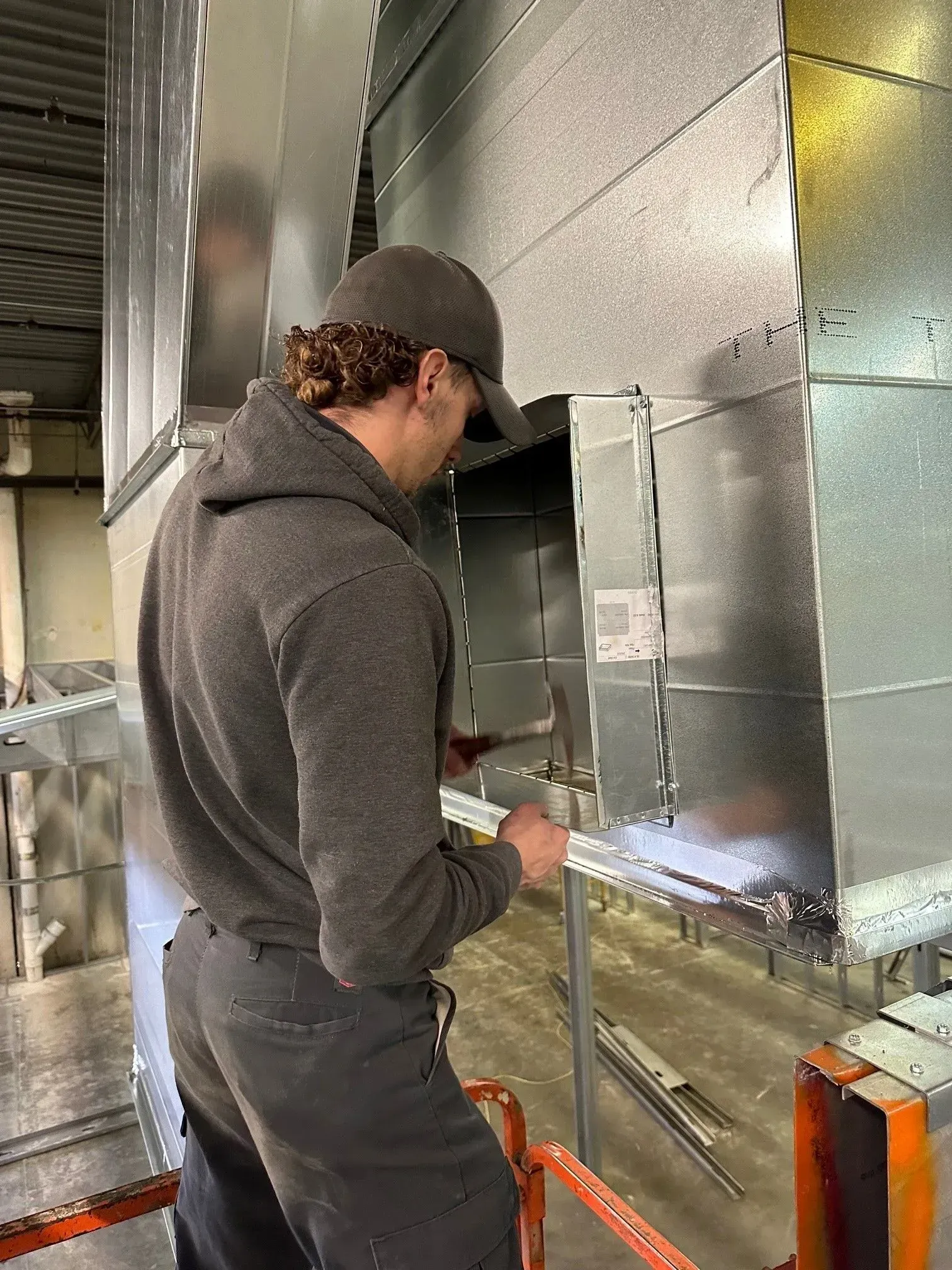 Person installing ductwork in a commercial building, using a ruler and tools.
