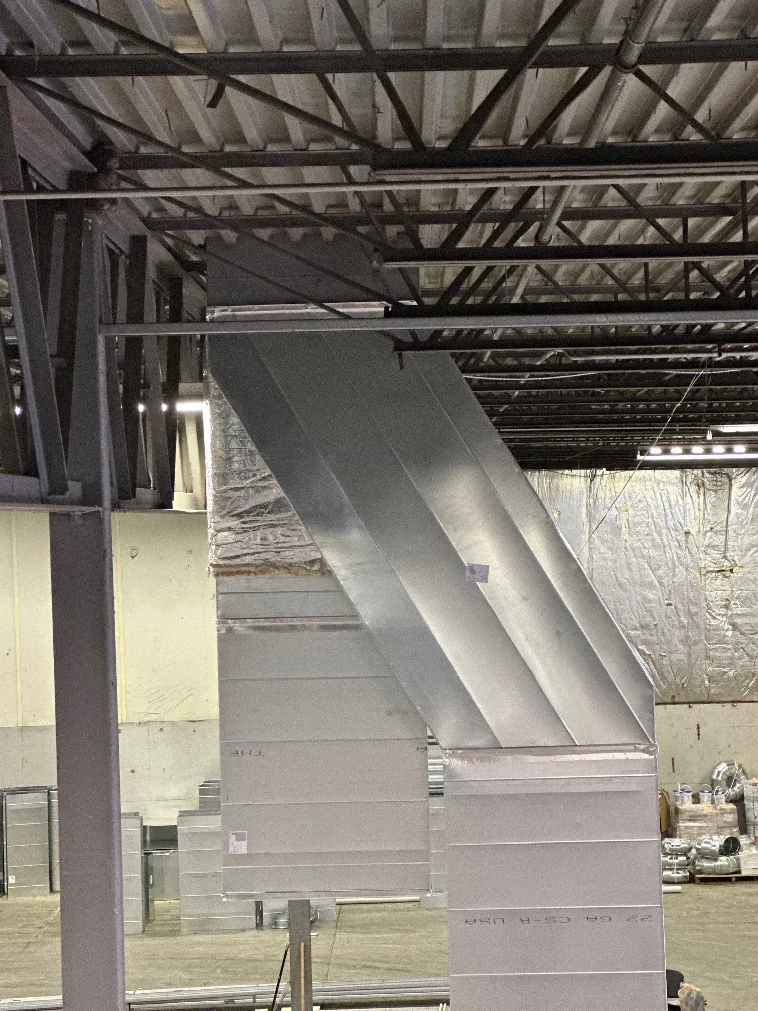 Metal ductwork angled across a ceiling in a commercial building with exposed beams and insulation.