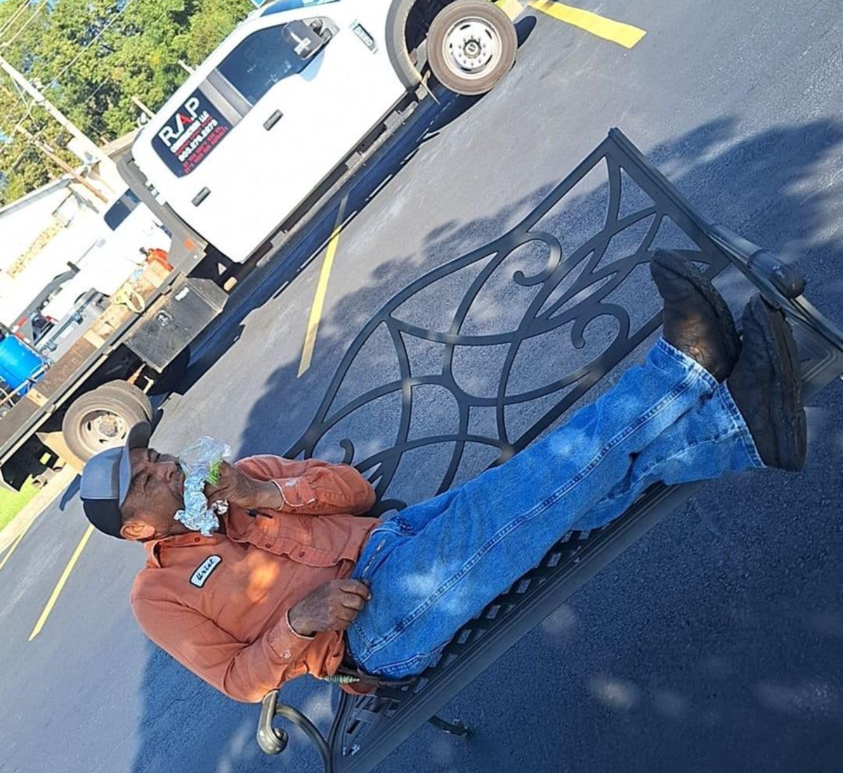 Man in orange work shirt and jeans resting on a bench next to a work truck.