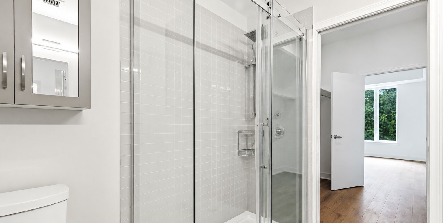 Bright white bathroom with glass shower and open door to a sunlit room beyond
