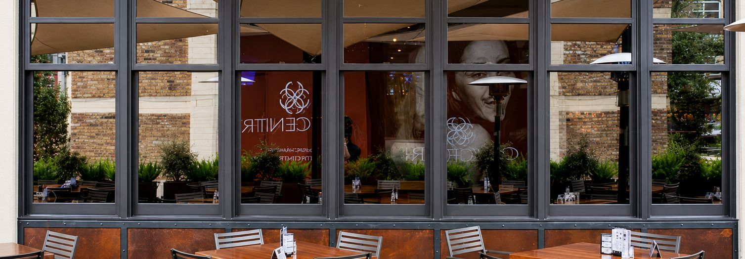 Large windowed storefront with potted plants and red wall decor behind the glass