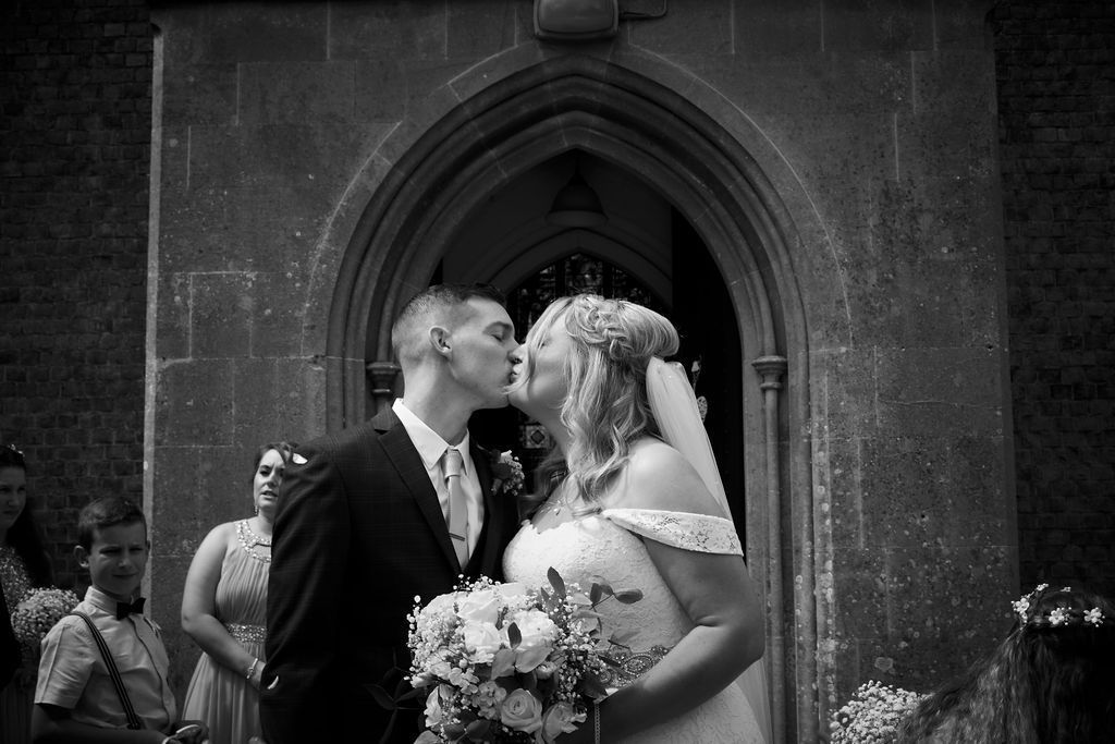 Bride and groom posing outside a brick building, bride holding a colorful bouquet and smiling