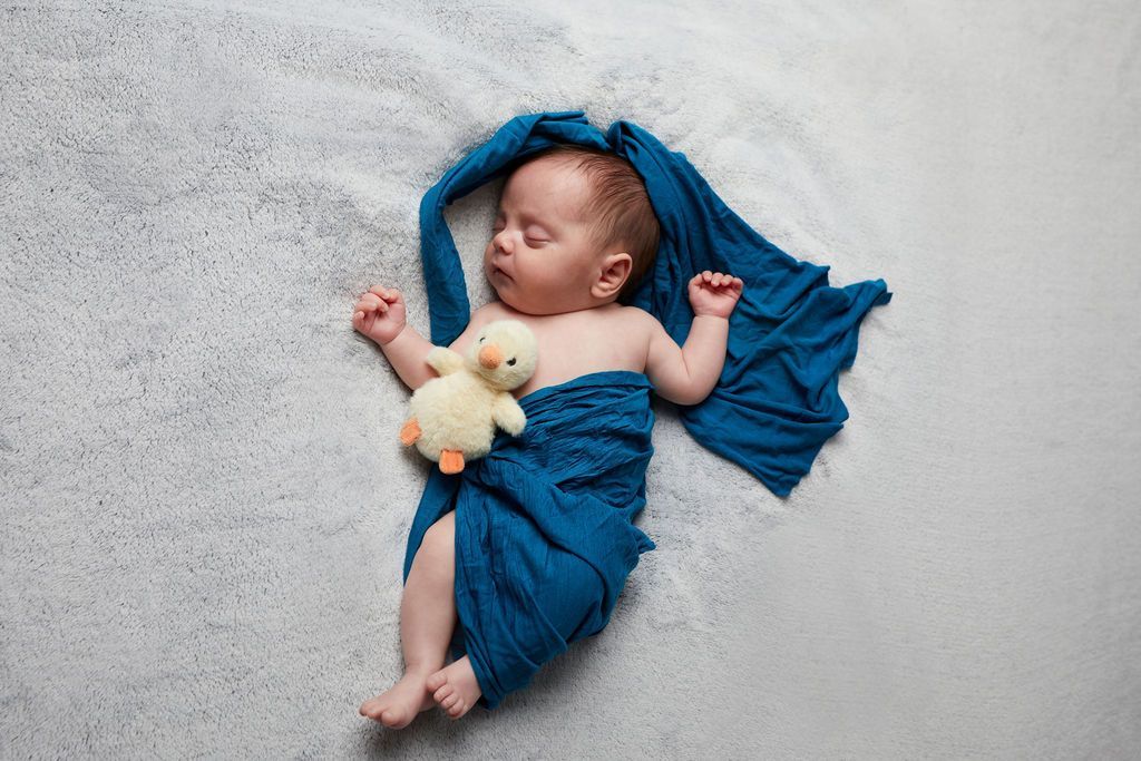 Sleeping newborn swaddled in teal fabric on a matching teal background