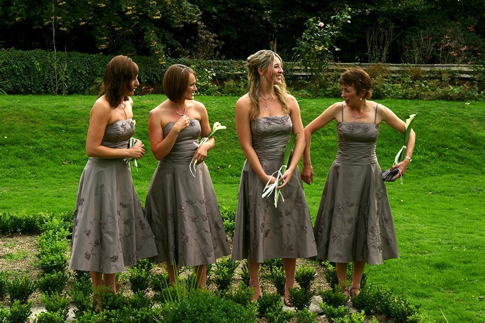 Four people in matching gray dresses standing in a grassy garden holding bouquets