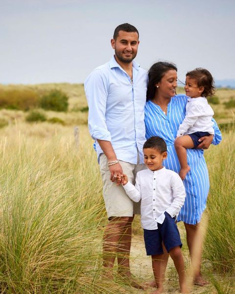 Family of four standing in tall grass, dressed in blue and white, with an overcast sky behind them.