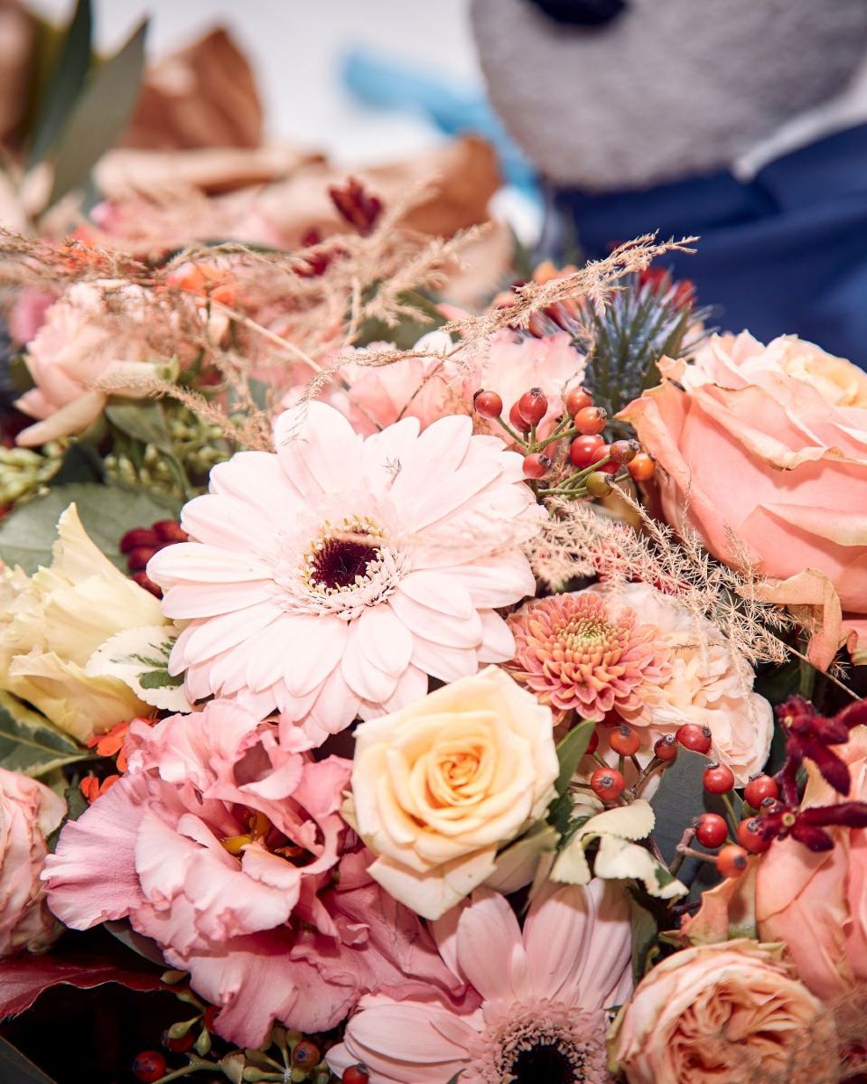 Bridal bouquet of red, pink, and white flowers held against a white wedding dress