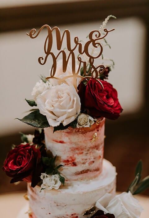 Two-tier wedding cake with red and white roses and a gold “Mr & Mrs” topper