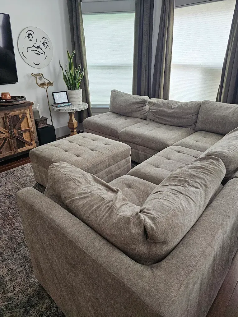 Living room with a large gray sectional sofa, ottoman, and round marble-top table with a laptop.