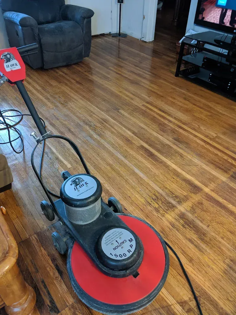 Floor buffer on wooden floor in a room, with a recliner and TV visible.
