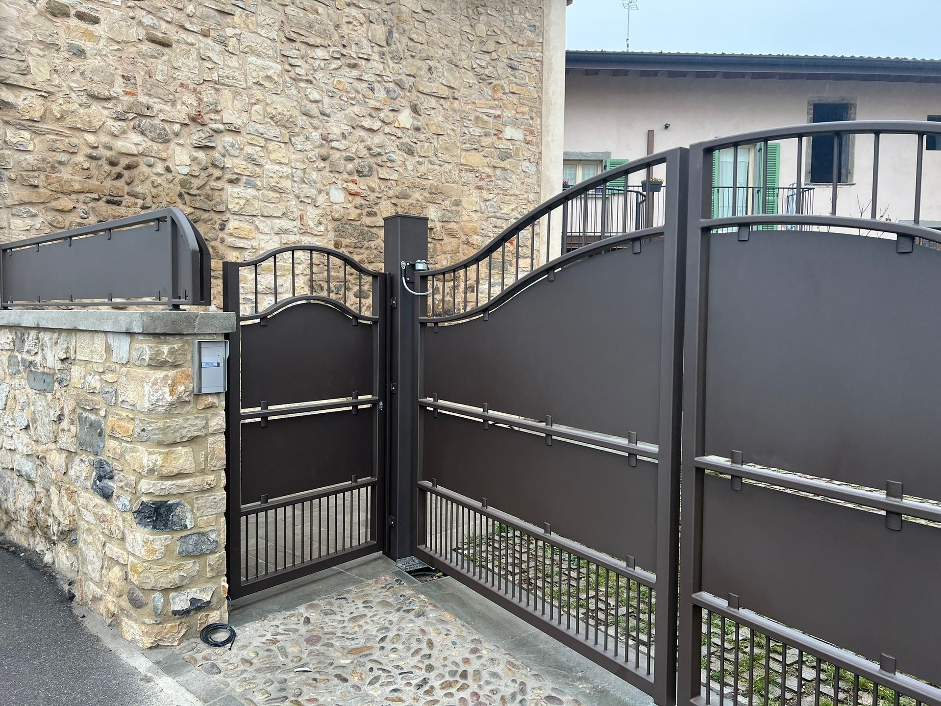 Cancello e recinzione in metallo nero accanto a un muro di pietra all'ingresso del vialetto.