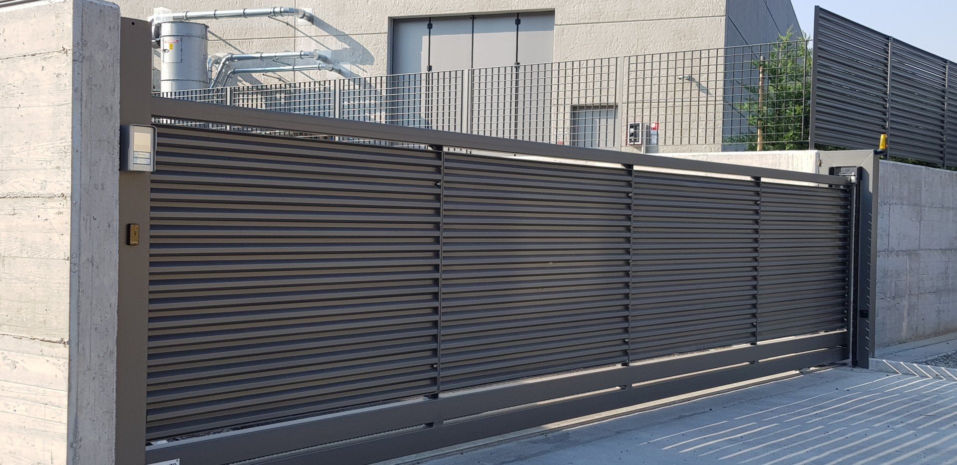 Esterno di una casa moderna con un lungo cancello scorrevole in metallo nero e un muro beige.