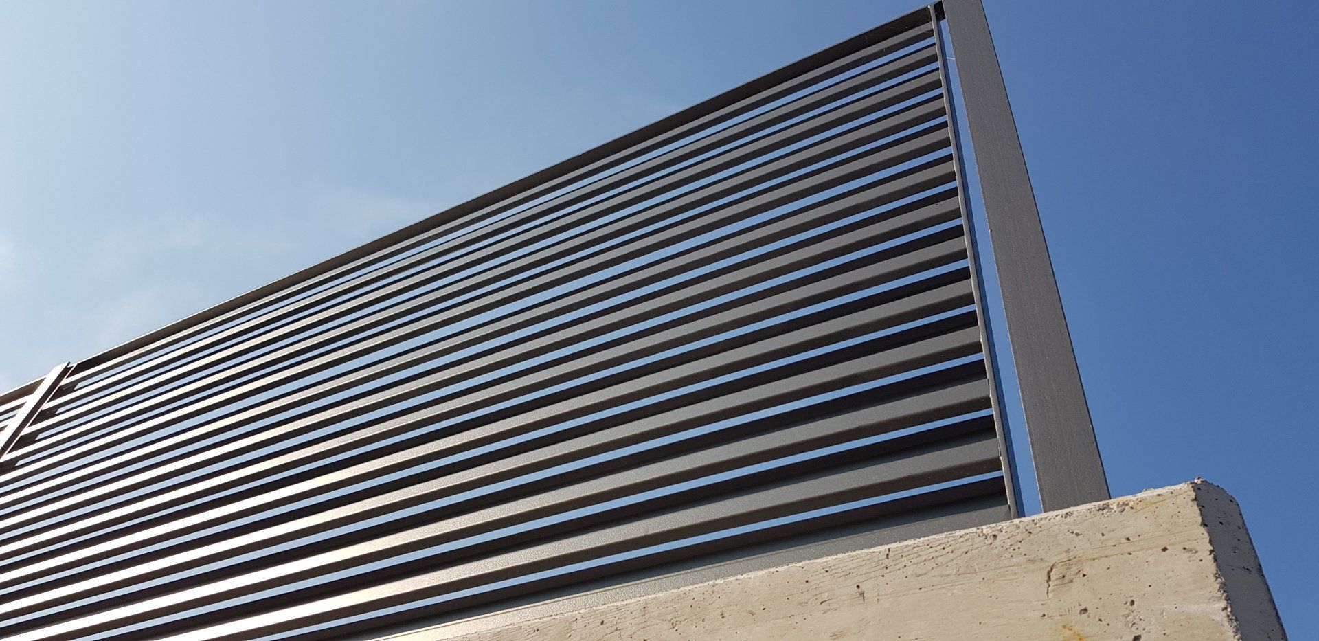 Veduta dal basso di un edificio moderno con finestre orizzontali scure su uno sfondo di cielo blu.