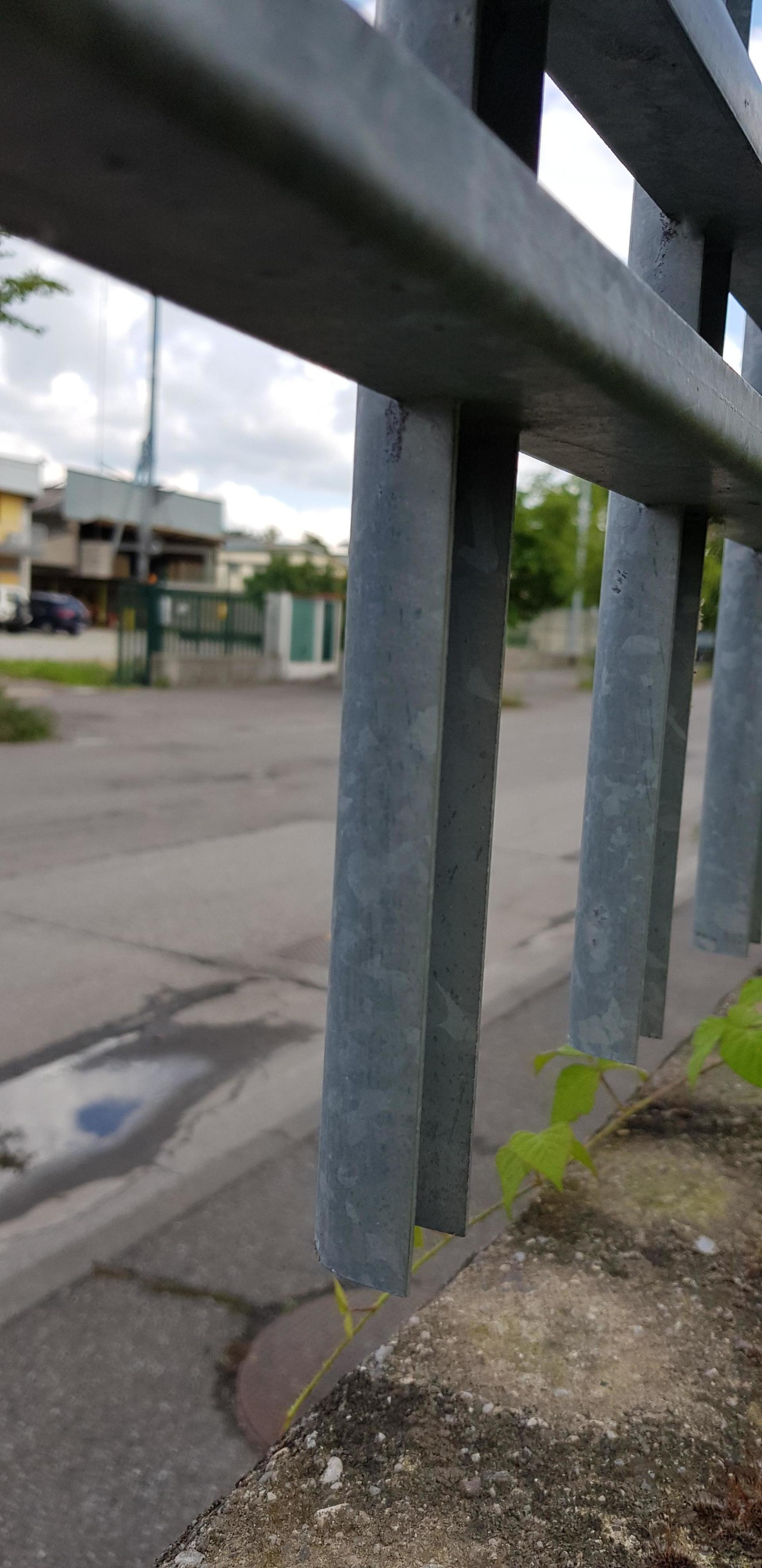 Primo piano di una ringhiera metallica piegata a lato di un marciapiede in una strada tranquilla.