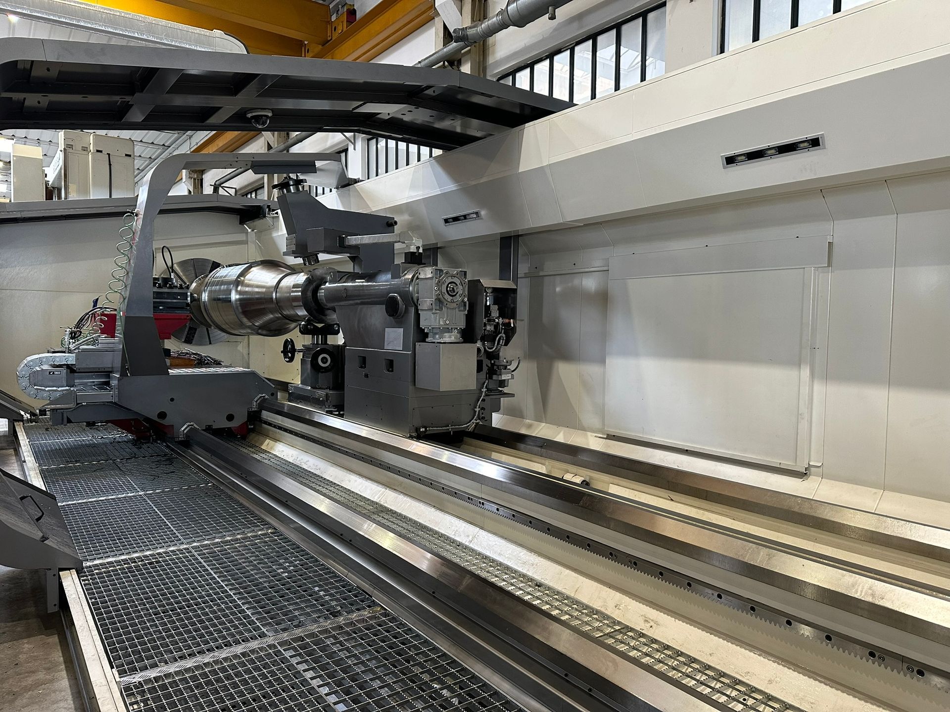 Macchinario industriale in una fabbrica, con binari metallici e una grande testa portautensili mobile.