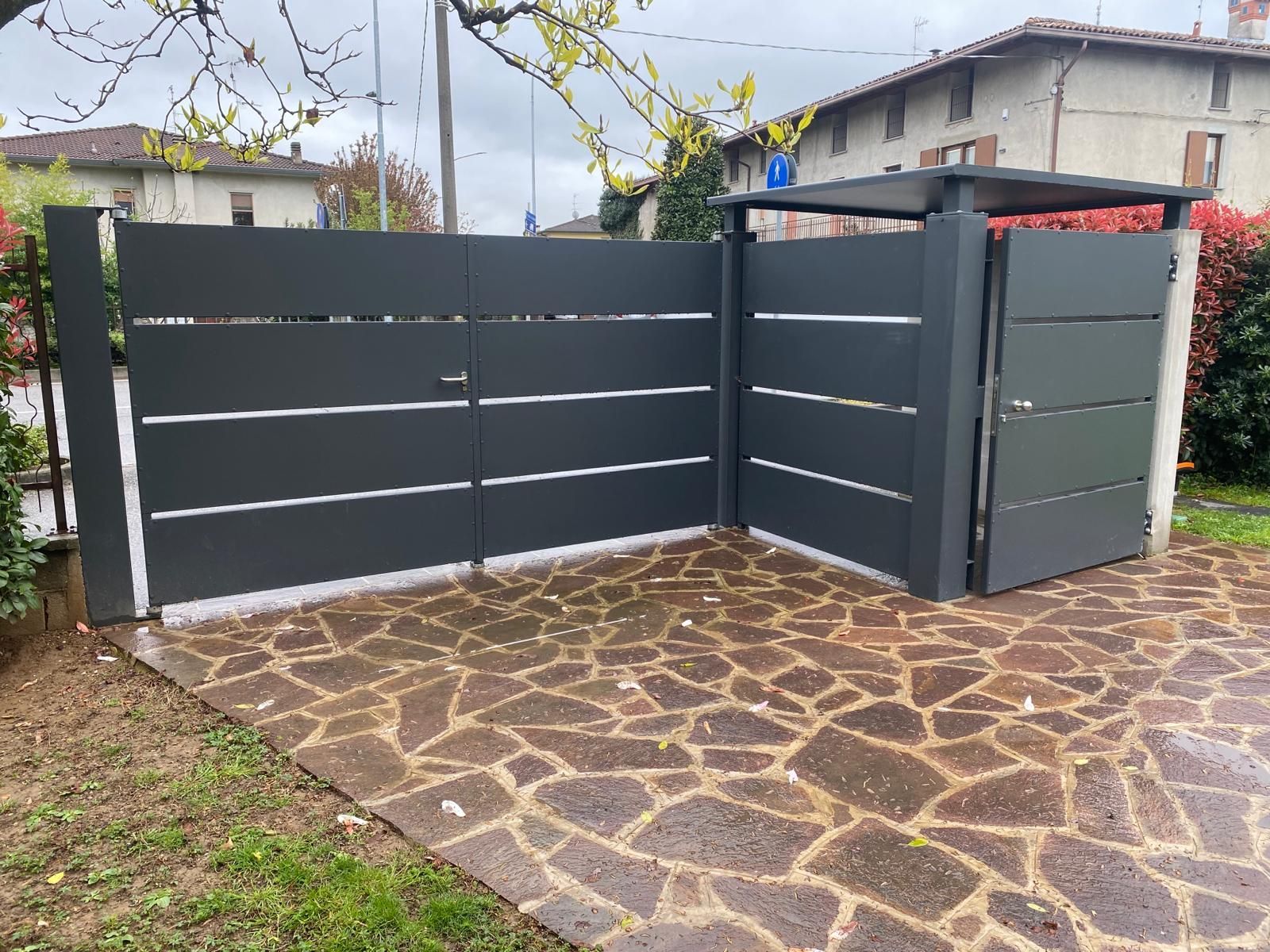 Cancello e recinzione moderni in metallo grigio accanto a un vialetto in pietra in un cortile