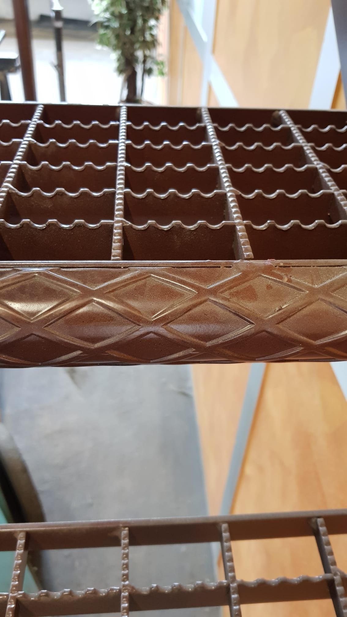 Primo piano della seduta e dello schienale di una sedia in metallo intrecciato marrone con un motivo decorativo a perline o a spirale bianca.