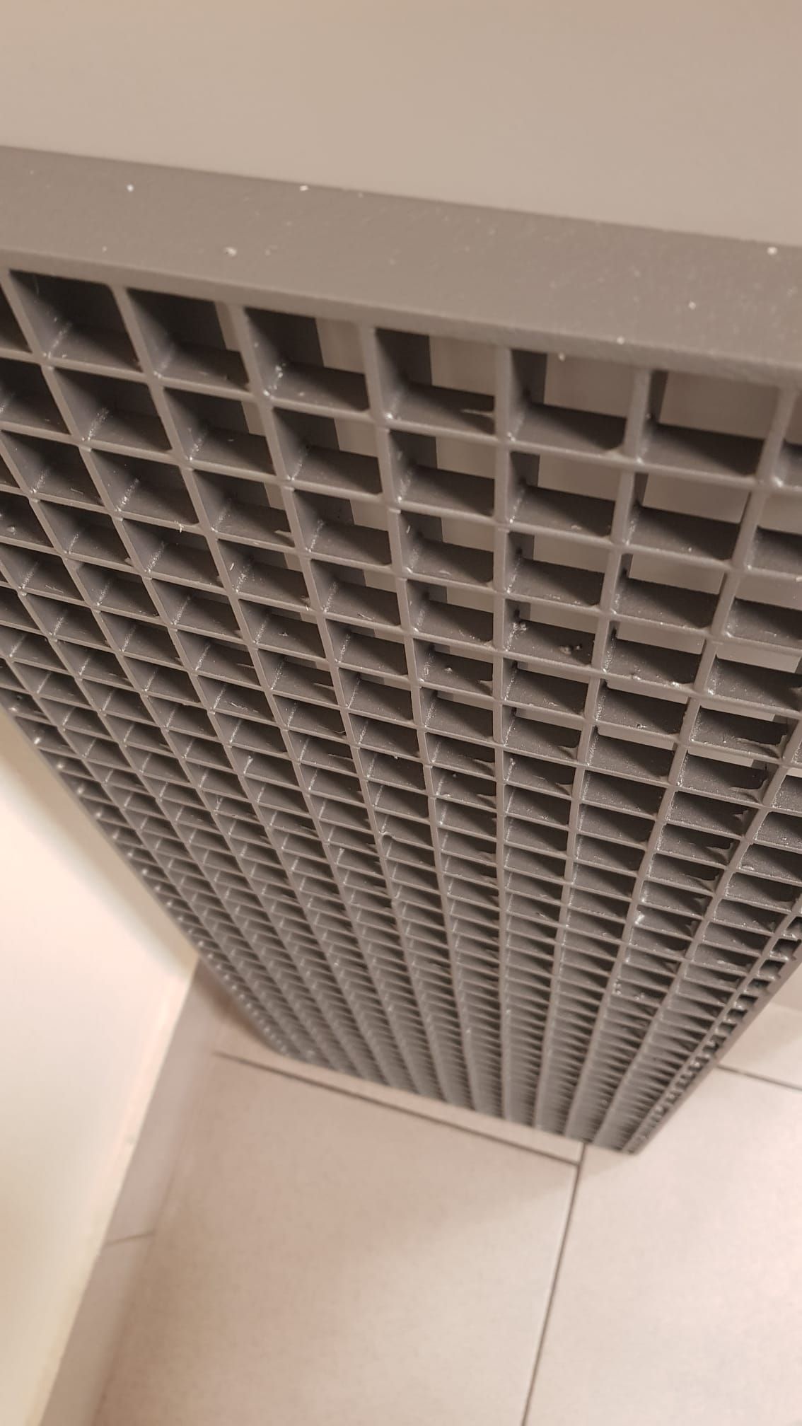 Primo piano di una griglia di ventilazione metallica grigia a soffitto in un angolo di una stanza bianca.