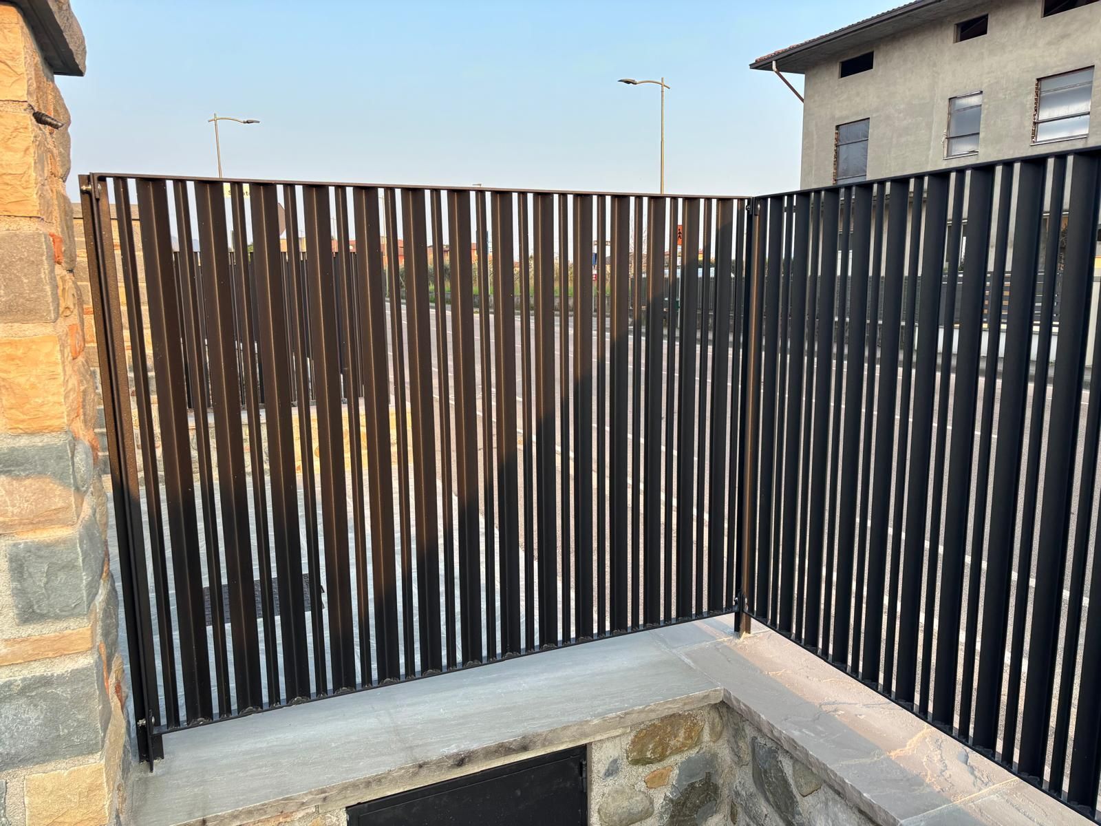 Patio esterno con recinzione a doghe nere e panchina in pietra in un angolo.
