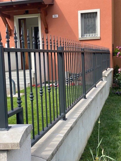 Una recinzione metallica nera costeggia un piccolo cortile anteriore accanto a una casa arancione con una finestra e una porta incorniciate di bianco.