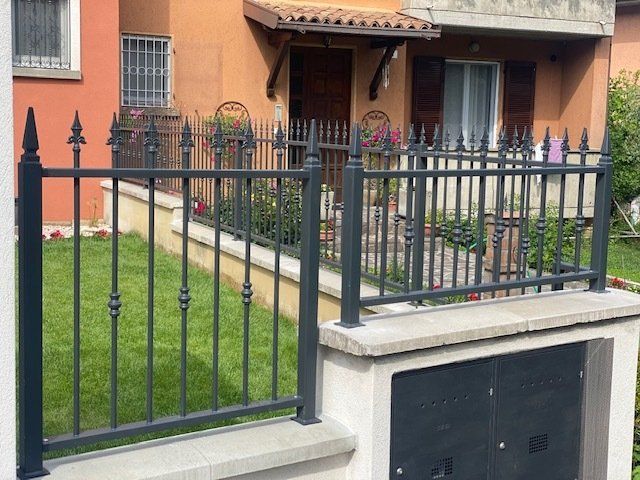 Recinzione in ferro nero attorno a un piccolo cortile erboso di fronte a una casa arancione con portico.