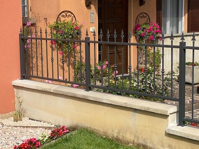 Balcone fiorito con ringhiera in ferro nero su un edificio color pesca.
