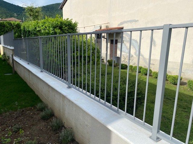 Ringhiera metallica lungo un vialetto di cemento accanto a una casa e a un giardino erboso.