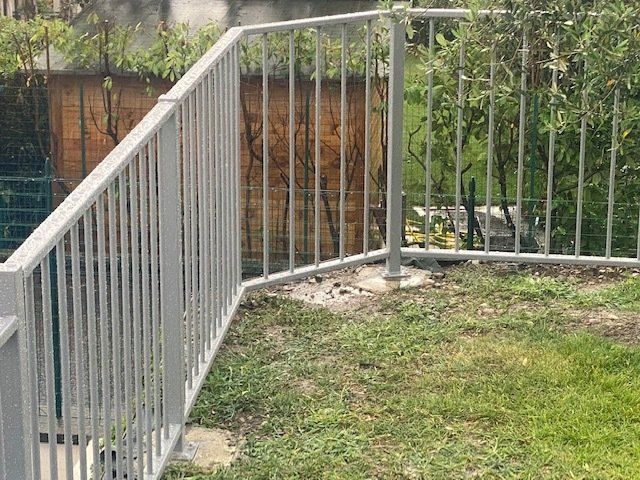 Ringhiera in metallo bianco lungo un sentiero erboso esterno accanto a un giardino o a un cortile.