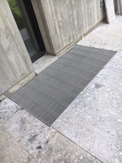 Ingresso in cemento con rampa in metallo grigio accanto a una parete dell'edificio e alla porta.
