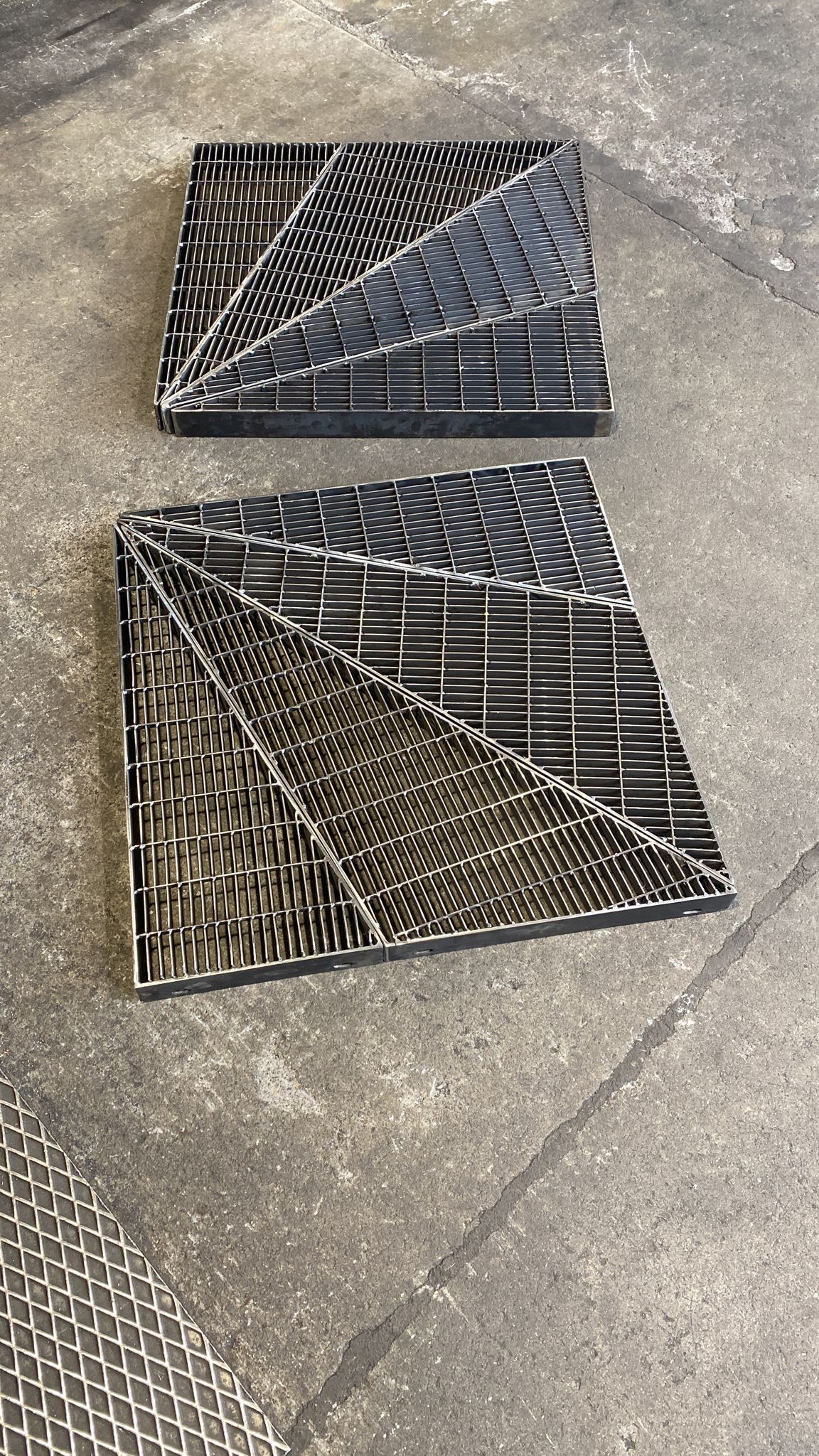 Due pezzi di tessuto nero con motivi geometrici adagiati su un pavimento di cemento grigio