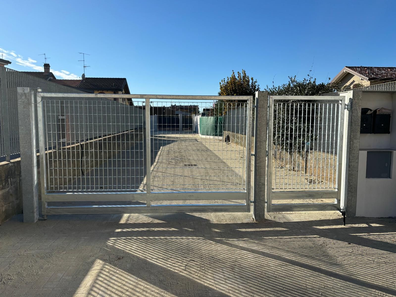 Cancello d'ingresso residenziale con recinzione in metallo bianco e vialetto d'accesso sotto un cielo azzurro limpido.