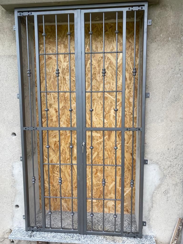 Porta blindata in metallo grigio sopra una finestra murata in un muro di stucco