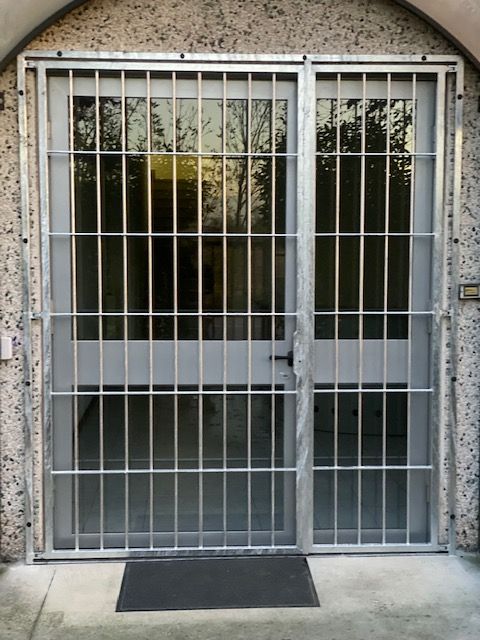 Cancello di sicurezza in metallo sopra un ingresso in vetro con un piccolo zerbino nero davanti