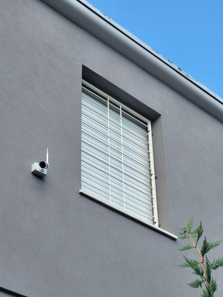 Parete grigia di un edificio con una finestra, persiane chiuse e una piccola telecamera di sicurezza montata accanto.