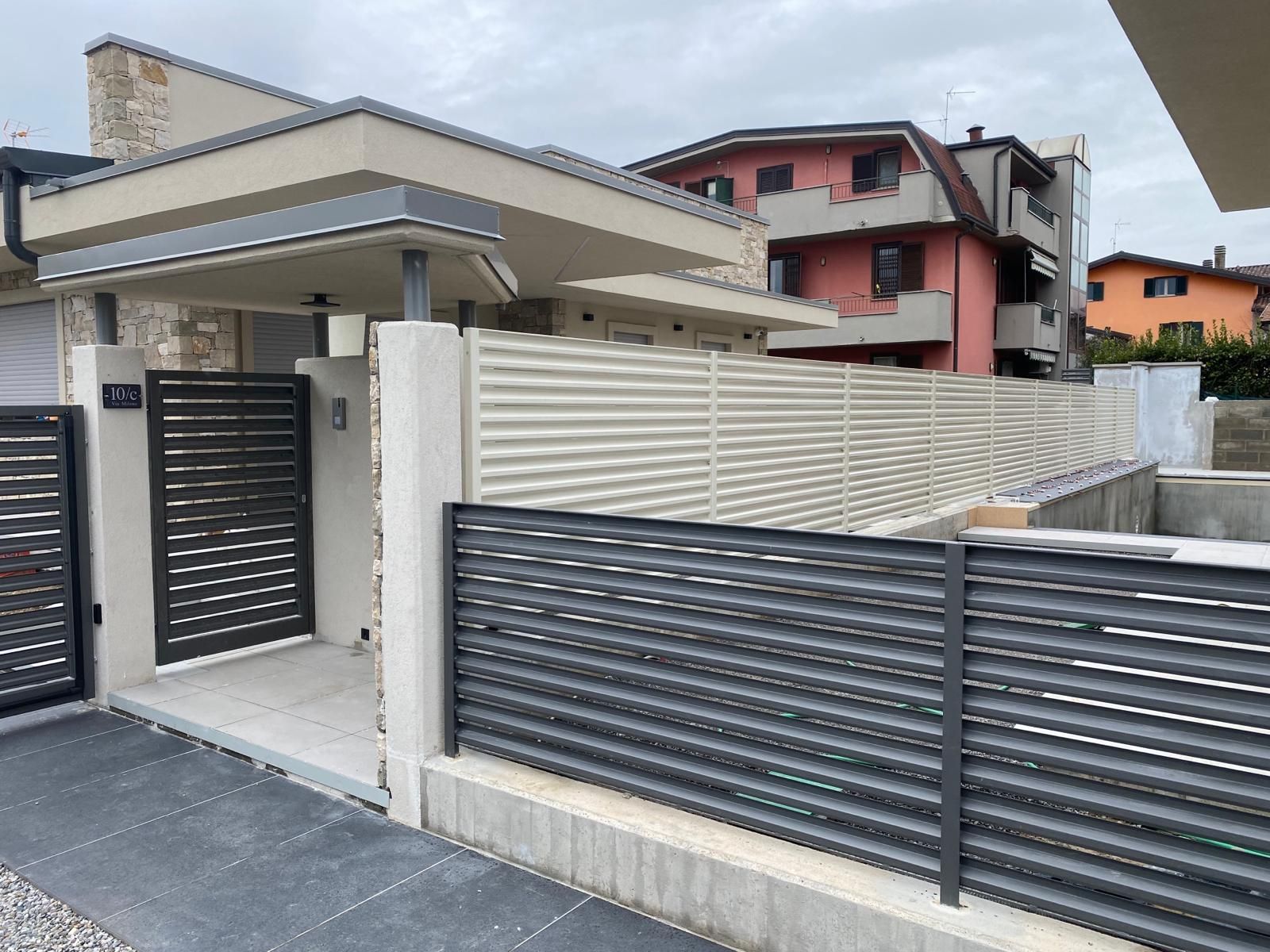 Esterno di una casa moderna con recinzione e cancello in bianco e nero lungo un vialetto pavimentato.