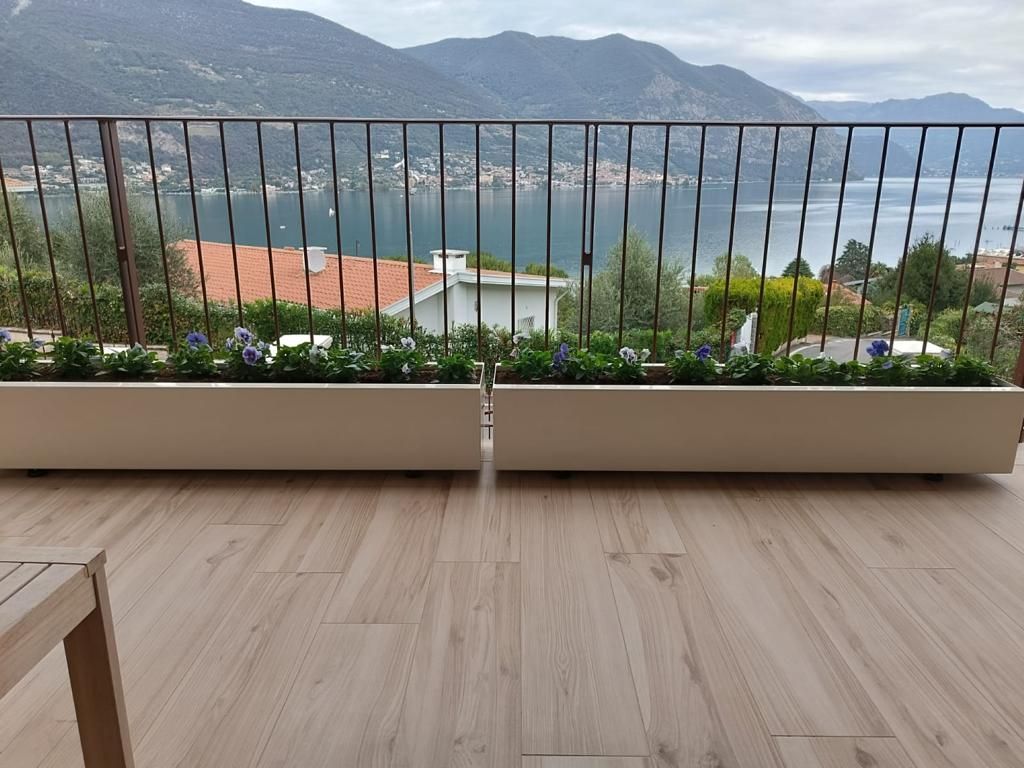 Balcone con pavimento in legno, ringhiera, fioriere e vista sul mare e sulle montagne.