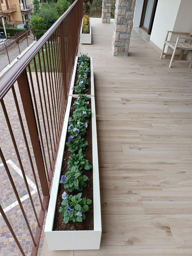 Stretto balcone con una lunga fioriera bianca accanto a una ringhiera in legno e pavimento in legno.