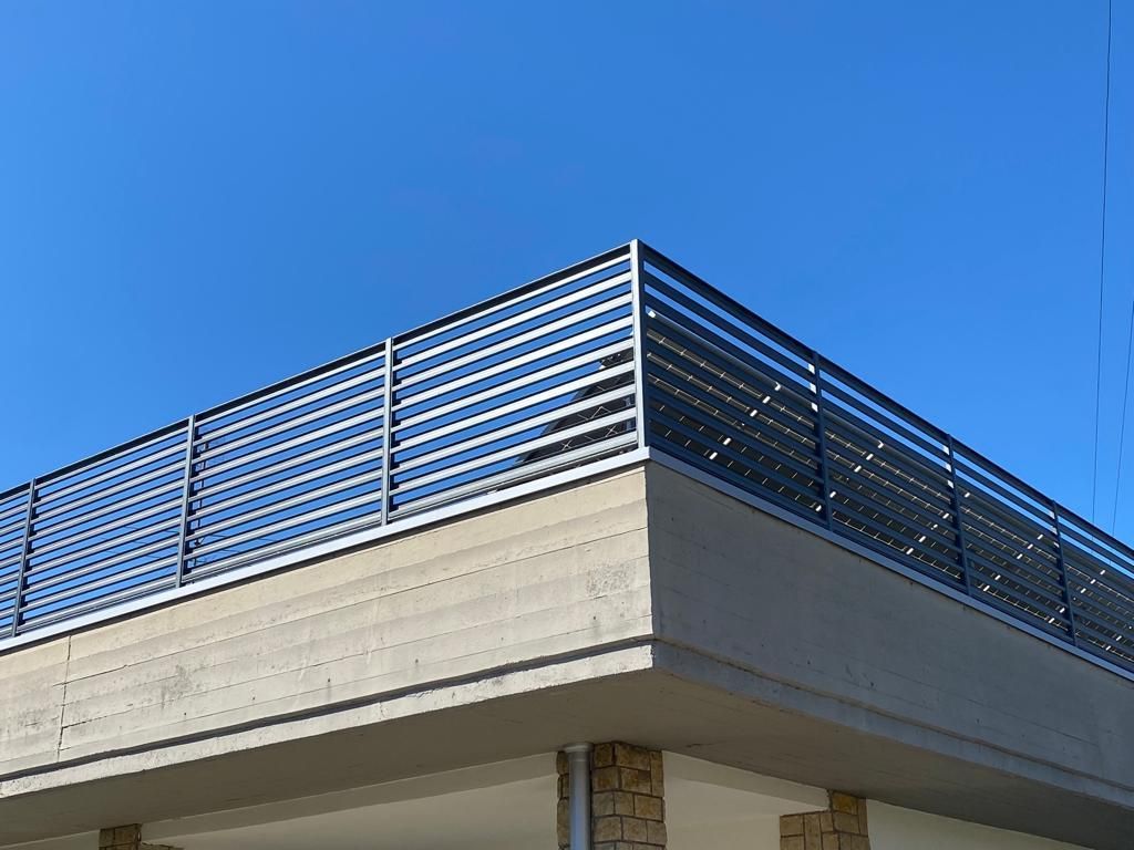 Tetto di un edificio moderno con ringhiera metallica sullo sfondo di un cielo azzurro limpido.