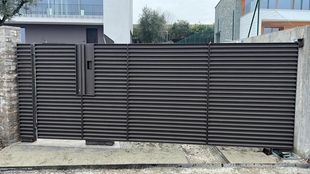 Cancello in metallo a doghe orizzontali marrone scuro con una piccola porta laterale davanti a una casa moderna.