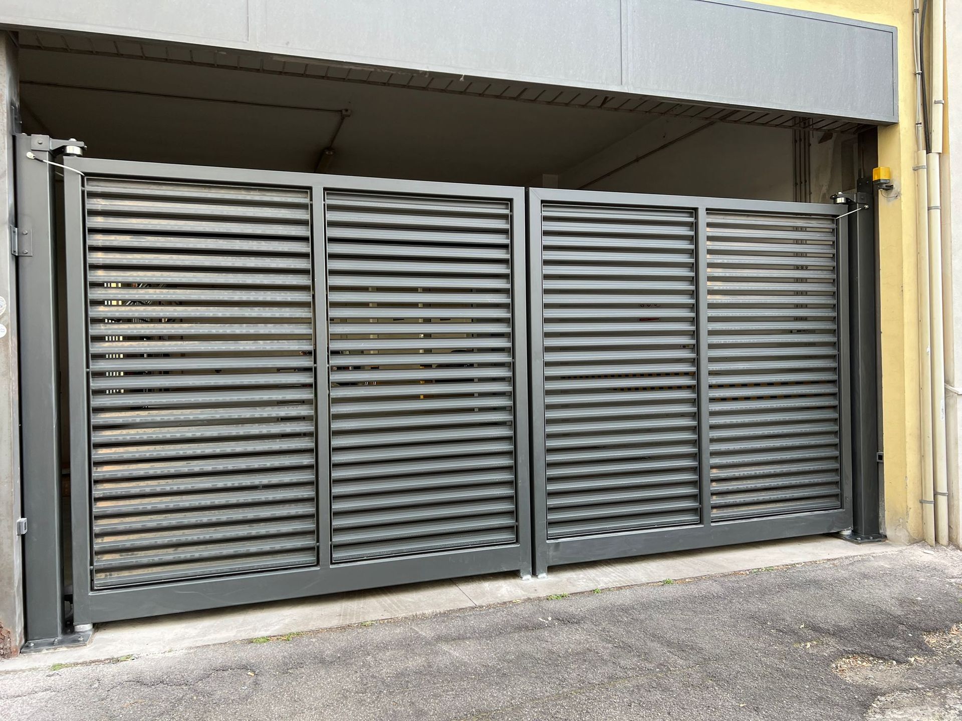 Cancello di sicurezza in metallo grigio all'ingresso di un magazzino, sotto una banchina di carico coperta.