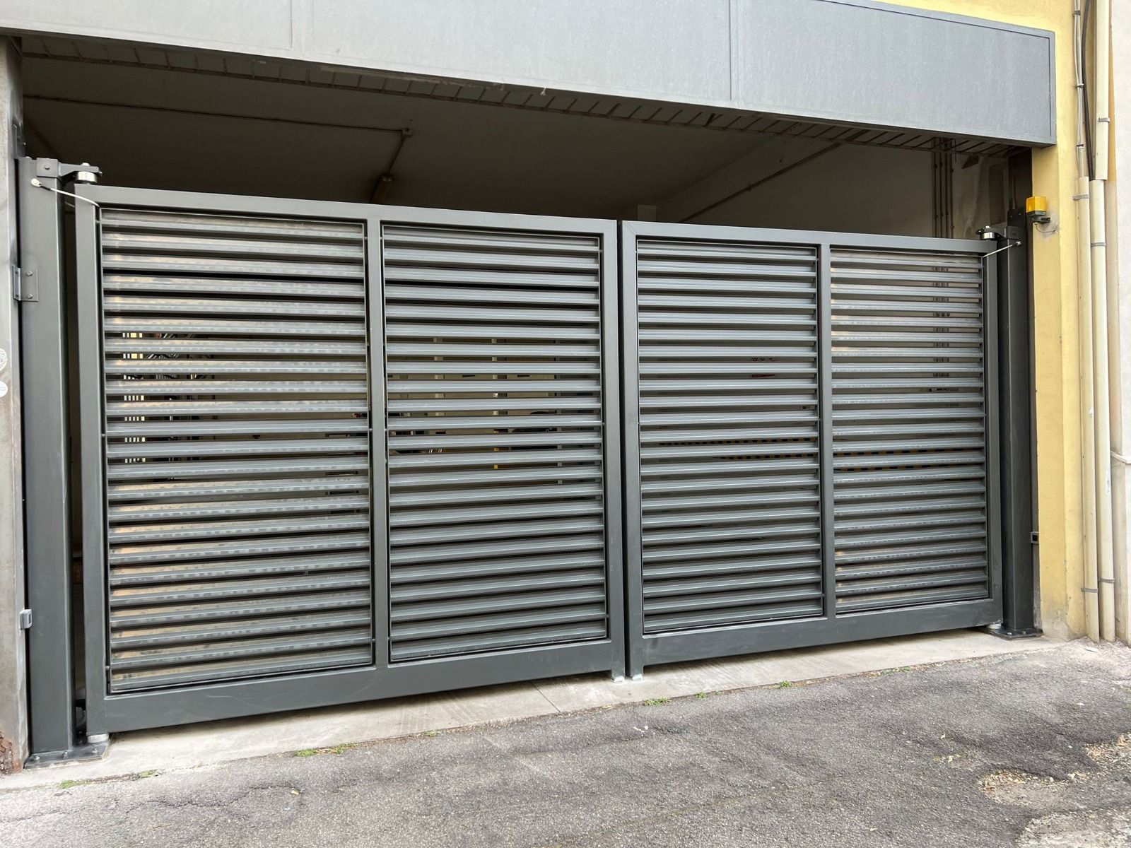 Cancello industriale grigio in metallo con lamelle orizzontali all'ingresso di un edificio.