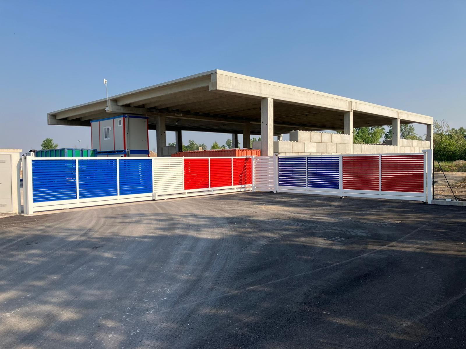 Cancelli metallici colorati davanti a una struttura esterna coperta su un lotto pavimentato.