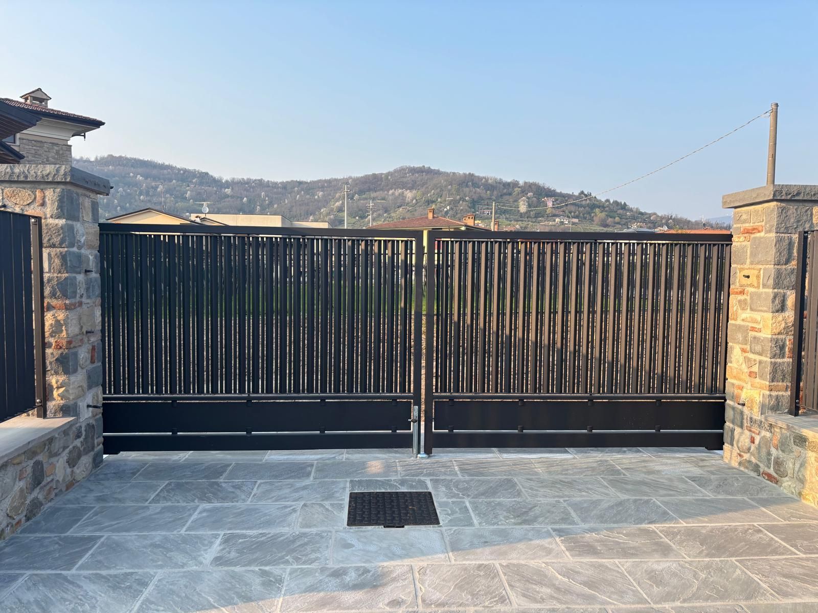Terrazza in pietra con cancello in metallo nero, fiancheggiata da pilastri, che si affaccia su colline lontane sotto un cielo limpido.