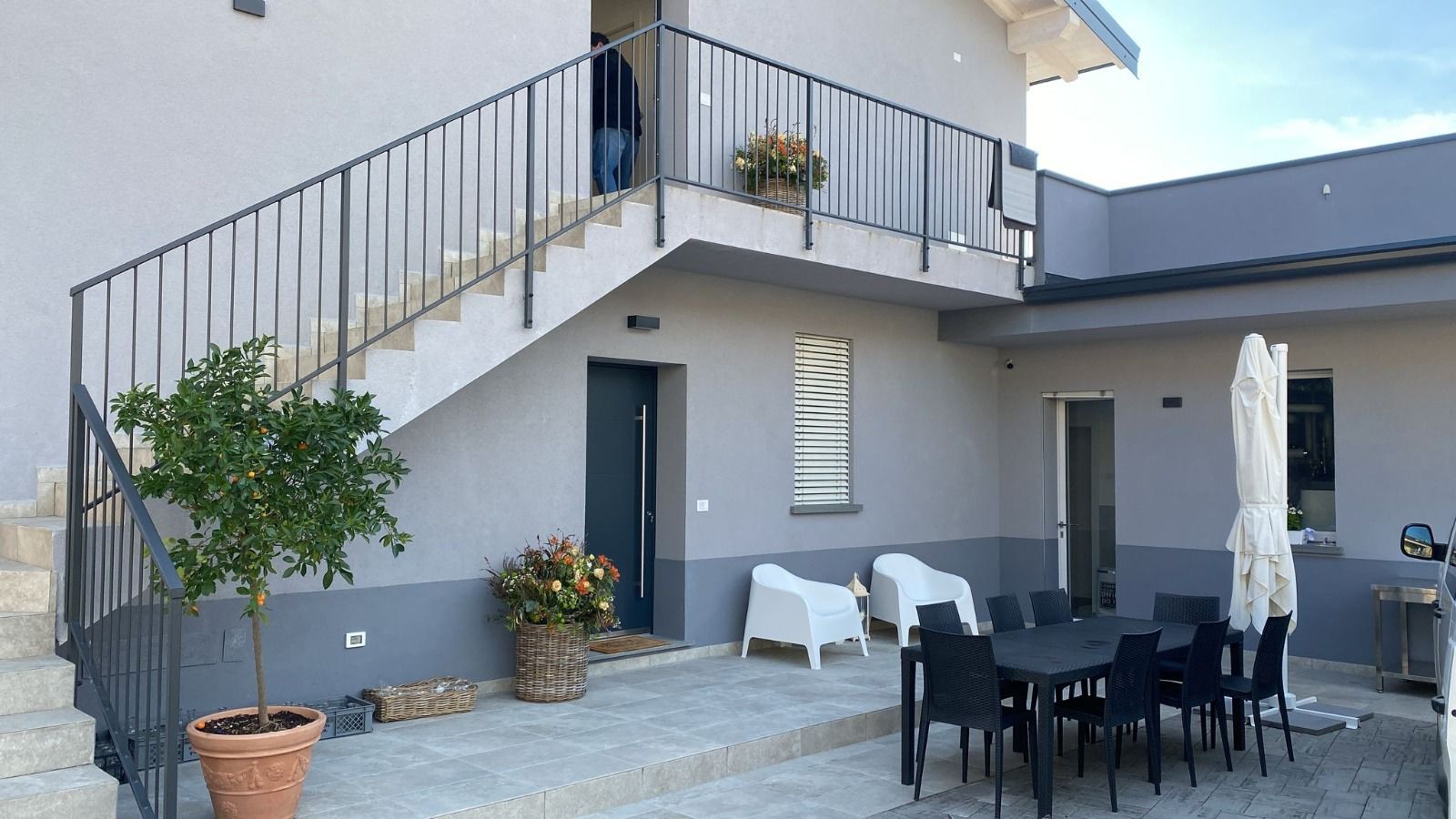 Cortile con patio, tavolo da pranzo all'aperto, sedie, piante in vaso e scala esterna accanto a una casa bianca.