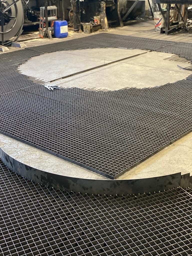 Piattaforma industriale con stuoia a rete nera che avvolge una struttura circolare in cemento.