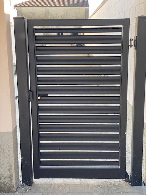 Cancello in metallo nero con lamelle orizzontali tra muri beige e un tetto di tegole sovrastante