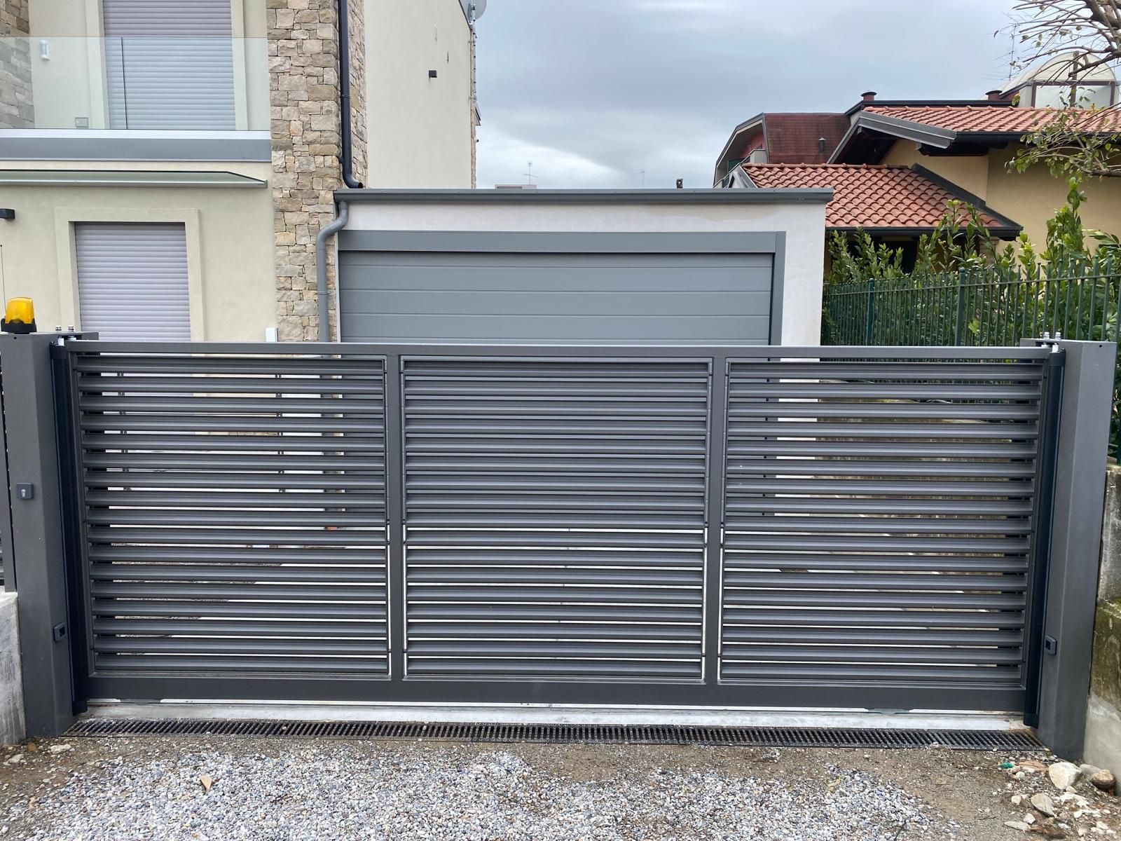 Cancello carrabile in metallo grigio davanti a una casa moderna con garage.